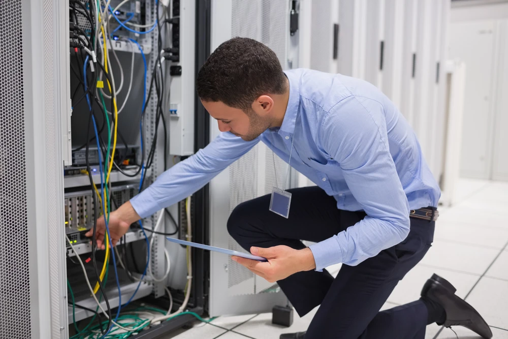 Intérieur d'un datacenter moderne avec un technicien informatique consultant un ordinateur portable devant des baies serveurs