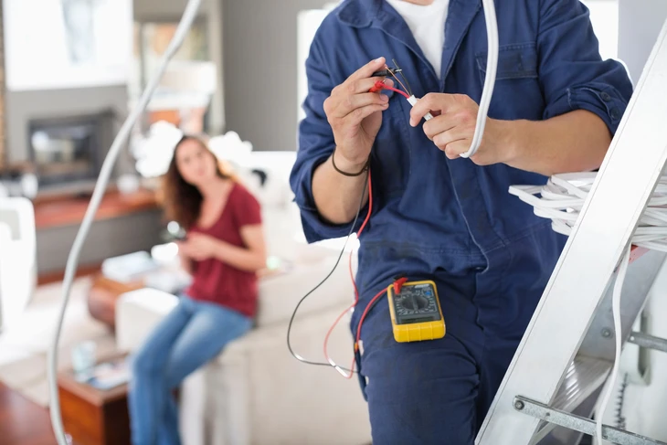 Intérieur d'installation électrique avec électricien utilisant multimètre numérique pour mesurer tension sur tableau de distribution