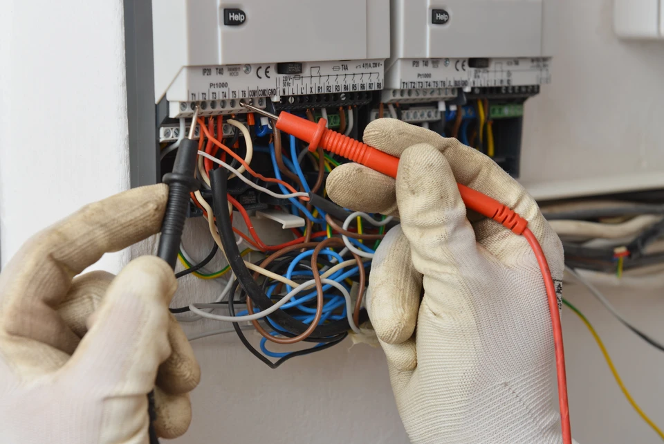 Technicien &eacute;lectricien portant des gants de protection travaillant sur un tableau &eacute;lectrique ouvert avec de nombreux c&acirc;bles color&eacute;s