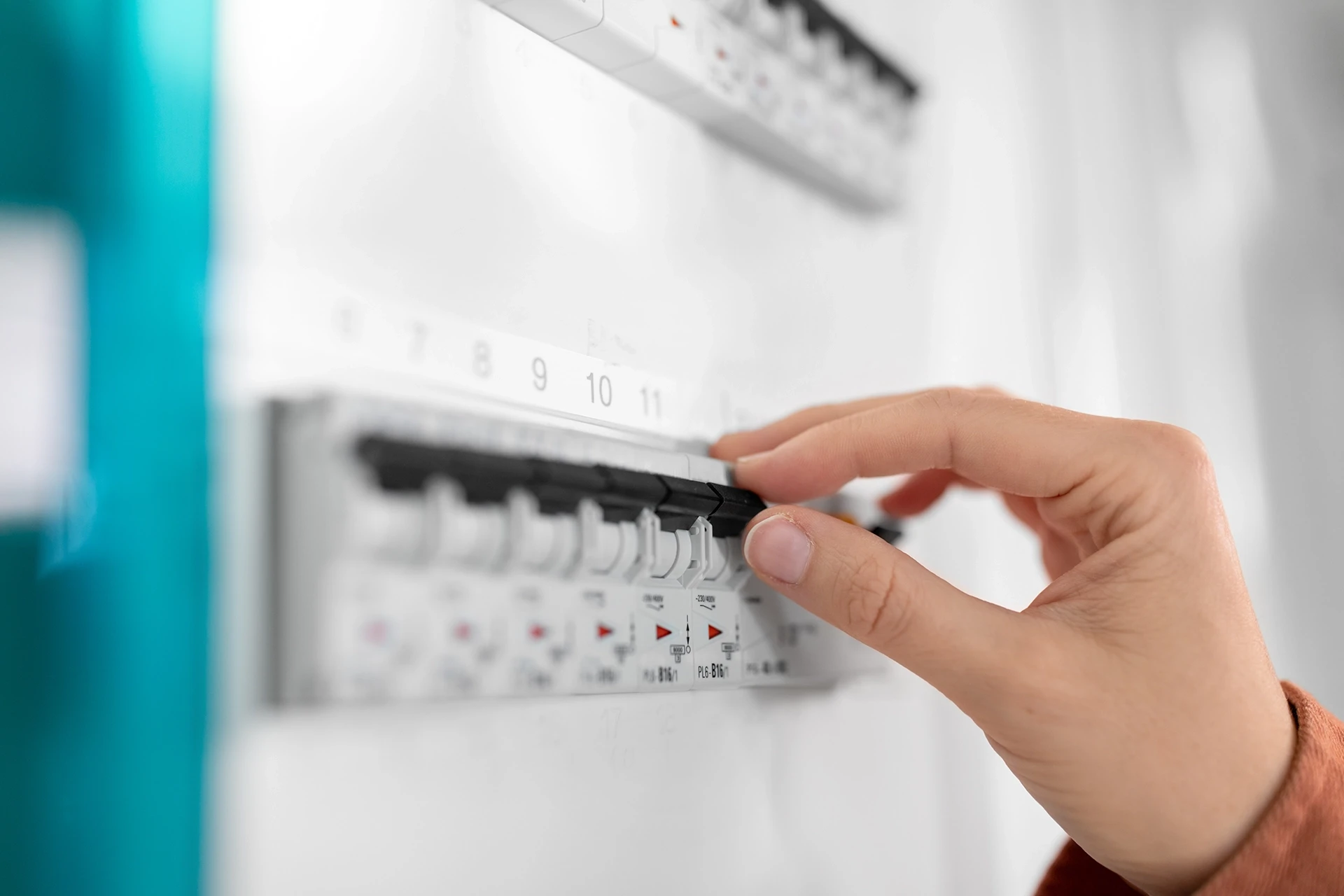 Électricien professionnel travaillant sur tableau électrique industriel, portant casque de sécurité blanc et lunettes de protection jaunes
